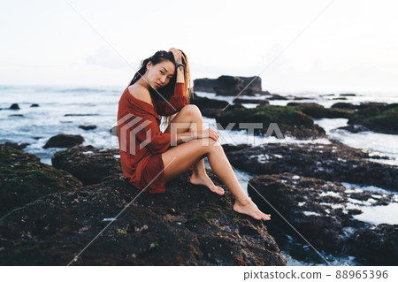 Young model in short dress sitting on shore rock 88965396