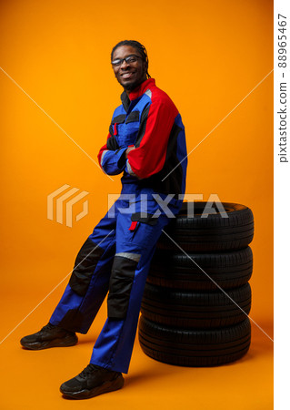 African american car service worker with car tyre against yellow background 88965467