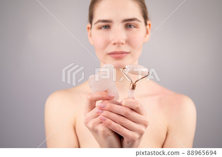 Caucasian woman holding pink roller massager and gouache scraper on white background. Caucasian woman holding pink roller massager and gouache scraper on white background. 88965694