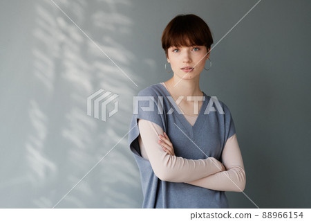 Portrait of serious young Caucasian woman in earrings standing with crossed arms against gray wall 88966154