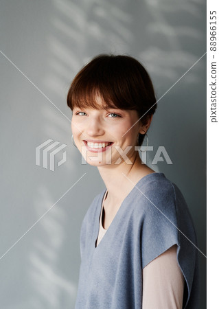 Happy attractive girl with short hair wearing cotton vest and earrings against gray wall Happy attractive girl with short hair wearing cotton vest and earrings against gray wall 88966155