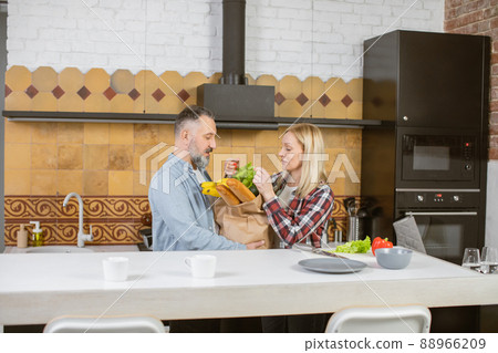 Mature married couple unpacking grocery bag on kitchen Mature married couple unpacking grocery bag on kitchen 88966209