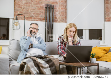 Man talking on mobile while woman typing on laptop at home Man talking on mobile while woman typing on laptop at home 88966247