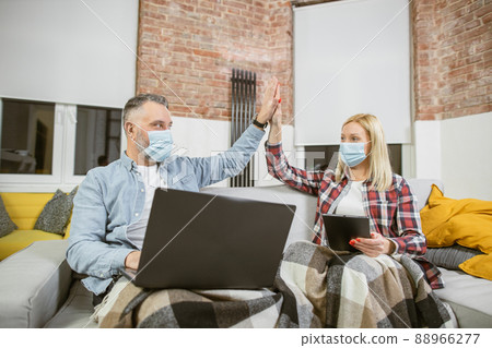 Mature couple in face masks with gadgets giving high five 88966277