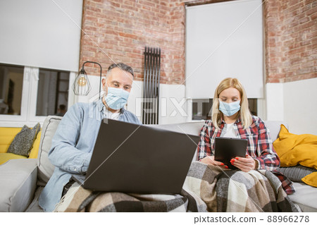 Family in face masks sitting on sofa with laptop and tablet 88966278