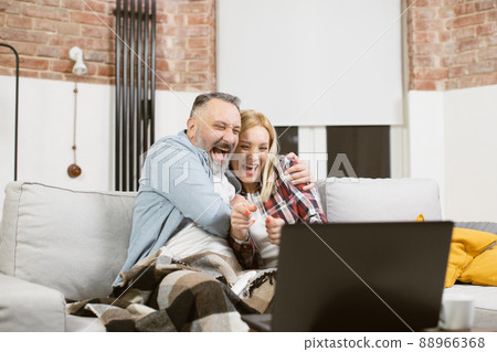 Cheerful mature family embracing on couch and using laptop Cheerful mature family embracing on couch and using laptop 88966368