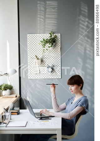 Busy attractive girl holding pencil and analyzing data on laptop while working in cozy home ofice Busy attractive girl holding pencil and analyzing data on laptop while working in cozy home ofice 88966498