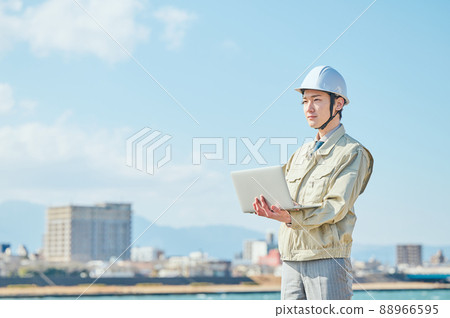 A young man in work clothes standing with a computer against the blue sky A young man in work clothes standing with a computer against the blue sky 88966595