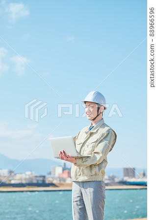 A young man in work clothes standing with a computer against the blue sky A young man in work clothes standing with a computer against the blue sky 88966596