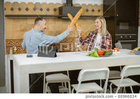Couple using baguettes for playful fight on bright kitchen Couple using baguettes for playful fight on bright kitchen 88966834