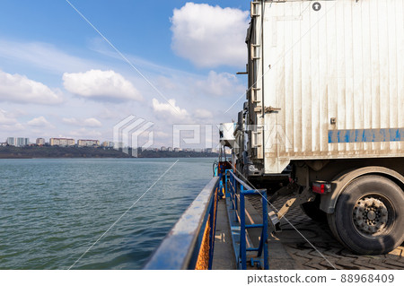 Close-up detail view of big industrial hopper truck body loaded on cargo ferry boat sailing on river or sea port blue sky day background. Freight logistics and comercial shipping transport vessel Close-up detail view of big industrial hopper truck body loaded on cargo ferry boat sailing on river or sea port blue sky day background. Freight logistics and comercial shipping transport vessel 88968409