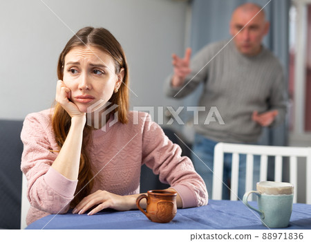 Sad woman sitting at table while her husband quarreling 88971836