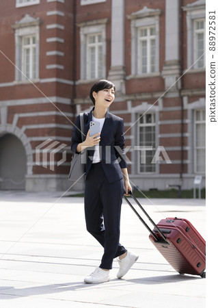 一個拿著智能手機的女商人，它拉著一個手提包走路 88972581