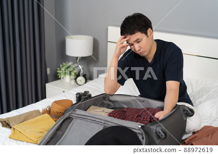 stressed man having problem with packing clothes into suitcase on bed, holiday travel concept stressed man having problem with packing clothes into suitcase on bed, holiday travel concept 88972619