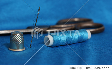 Spool of Blue Thread, Thimble and Needle on Blue Fabric Spool of Blue Thread, Thimble and Needle on Blue Fabric 88973356