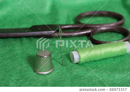 Spool of Green Thread, Thimble and Needle on Green Fabric Spool of Green Thread, Thimble and Needle on Green Fabric 88973357