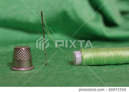 Spool of Green Thread, Thimble and Needle on Green Fabric Spool of Green Thread, Thimble and Needle on Green Fabric 88973358