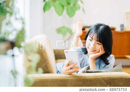 A woman lying on the sofa and holding a smartphone A woman lying on the sofa and holding a smartphone 88973733