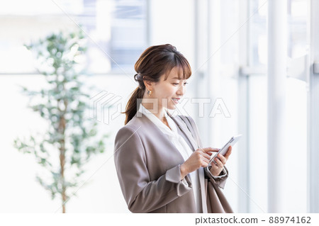 A business woman standing by a bright window with a smartphone A business woman standing by a bright window with a smartphone 88974162