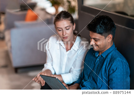 Multiethnic business people man with a female colleague working together on tablet computer in relaxation area of modern startup office Multiethnic business people man with a female colleague working together on tablet computer in relaxation area of modern startup office 88975144