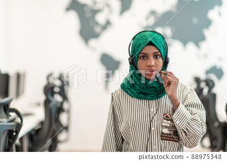 Muslim female with green hijab scarf customer representative business woman with phone headset helping and supporting online with customer in modern call centre Muslim female with green hijab scarf customer representative business woman with phone headset helping and supporting online with customer in modern call centre 88975348