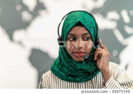 Afro Muslim female with green hijab scarf customer representative business woman with phone headset helping and supporting online with customer in modern call centre Afro Muslim female with green hijab scarf customer representative business woman with phone headset helping and supporting online with customer in modern call centre 88975349