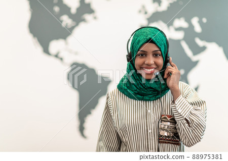 Afro Muslim female with green hijab scarf customer representative business woman with phone headset helping and supporting online with customer in modern call centre 88975381