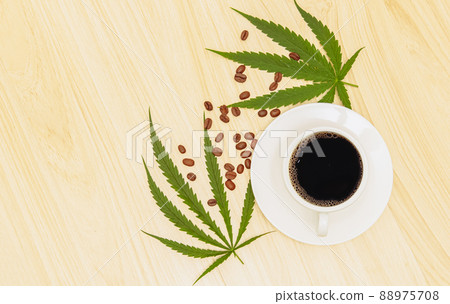Hot black coffee in a cup with a white saucer and coffee beans sprinkled on a wooden table and decorated with hemp leaves, cannabis coffee relaxing drink concept.flat lay,top-down,top view. Hot black coffee in a cup with a white saucer and coffee beans sprinkled on a wooden table and decorated with hemp leaves, cannabis coffee relaxing drink concept.flat lay,top-down,top view. 88975708