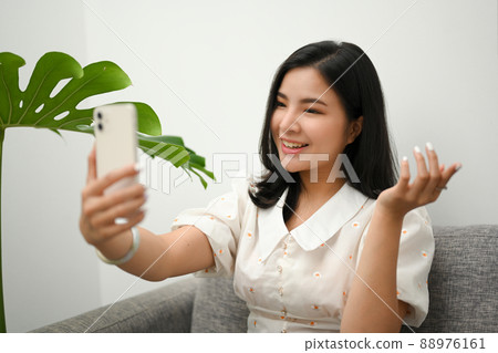Charming Asian young woman taking herself photography via her smartphone Charming Asian young woman taking herself photography via her smartphone 88976161