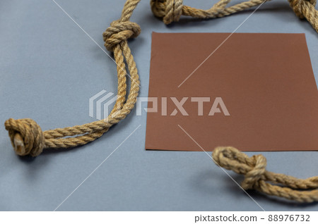 A ship's rope with knots and a brown empty square against a gray background. View from above at an angle. Close-up. Selective focus. 88976732