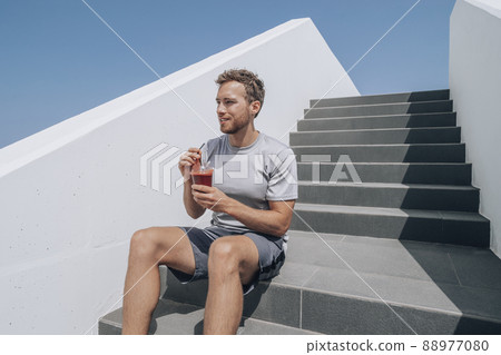 Man drinking healthy smoothie detox juice post cardio workout at gym stairs. Runner athlete living an active lifestyle Man drinking healthy smoothie detox juice post cardio workout at gym stairs. Runner athlete living an active lifestyle 88977080