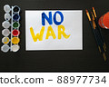 Man paints poster for rally with the slogan NO TO WAR. With brush and paints, he prints colorful bright letters on sheet. Person's requirement. Poster with call, rally, picket, march, protest, action 88977734