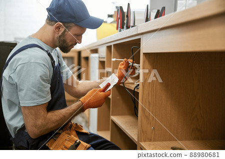 Bearded young man repairing desk electrical wires Bearded young man repairing desk electrical wires 88980681