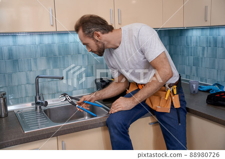 Young caucasian man working with sink sitting on tabletop Young caucasian man working with sink sitting on tabletop 88980726
