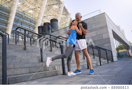 Full length shot of lovely sportive middle aged couple, man and woman in sportswear embracing while standing together outdoors Full length shot of lovely sportive middle aged couple, man and woman in sportswear embracing while standing together outdoors 88980813