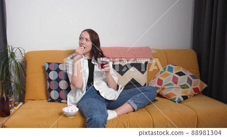A pregnant girl drinks alcohol on the couch and eats marshmallows. A young woman is pregnant. Early pregnancy 88981304