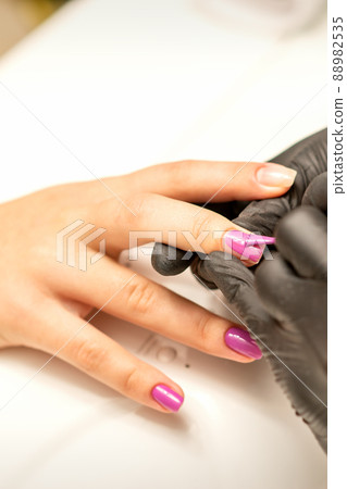 Professional manicure. A manicurist is painting the female nails of a client with purple nail polish in a beauty salon, close up. Beauty industry concept Professional manicure. A manicurist is painting the female nails of a client with purple nail polish in a beauty salon, close up. Beauty industry concept 88982535