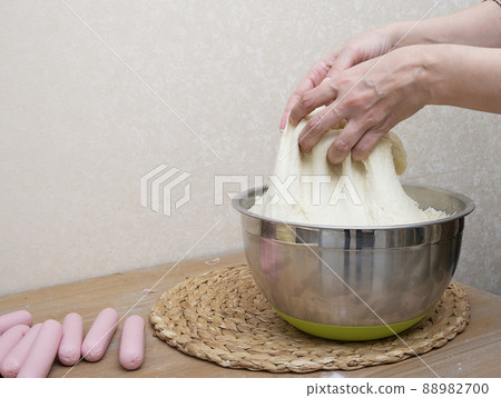 Women's hands are kneading the dough in the home kitchen for making hot dogs - close-up of women's hands. Mastery of cooking at home. Women's hands are kneading the dough in the home kitchen for making hot dogs - close-up of women's hands. Mastery of cooking at home. 88982700