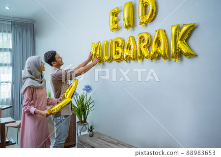 muslim couple decorating their house with eid mubarak text on the wall muslim couple decorating their house with eid mubarak text on the wall 88983653