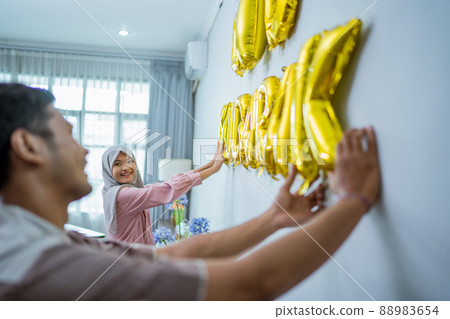 muslim couple decorating their house with eid mubarak text on the wall muslim couple decorating their house with eid mubarak text on the wall 88983654