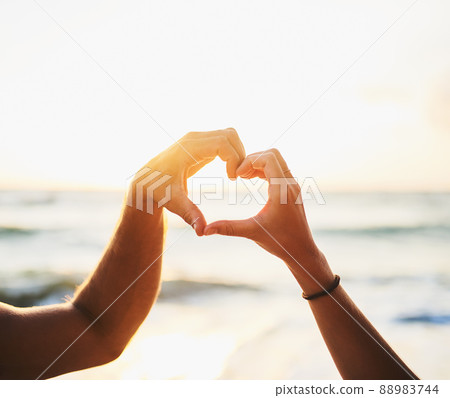 Love starts with me and you. Cropped shot of a couple forming a heart shape with their hands at the beach. 88983744