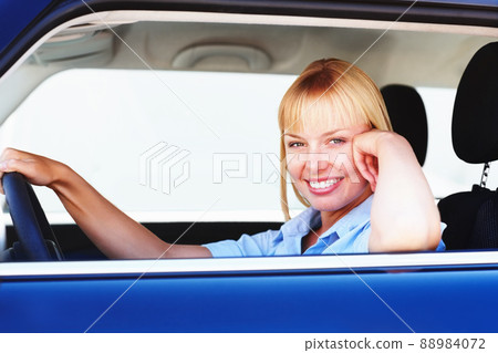 Pretty woman smiling from the drivers seat of a car. Smiling blond woman in a car sitting at the drivers seat. 88984072