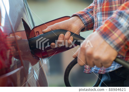 Male model stands by an electric car and holds a charging plug 88984621