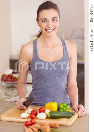 She enjoys food and loves cooking. Portrait of a beautiful young woman chopping up vegetables in the kitchen. 88984752