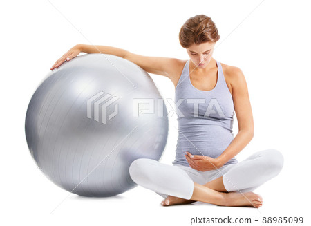 Taking care of her baby before its born. A fit pregnant woman gazing down at her stomach while holding an exercise ball. 88985099