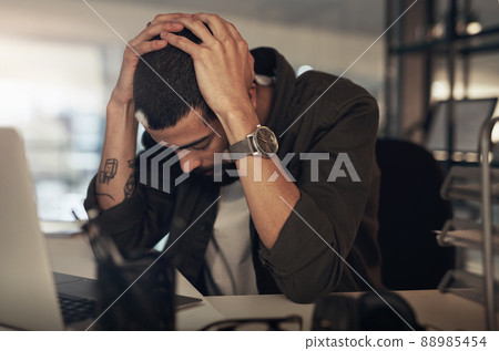 Stress will wear you down if you let it. Shot of a young businessman feeling stressed while working late at night in a modern office. 88985454