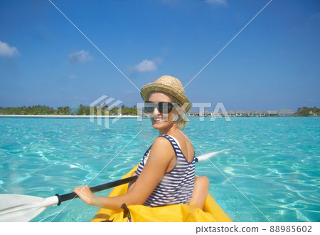 Paddling towards the beach. A beautiful young woman paddling on a boat in a tropical ocean. Paddling towards the beach. A beautiful young woman paddling on a boat in a tropical ocean. 88985602