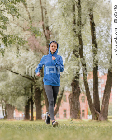 a European woman in a blue hoodie is running and doing sports in the park. fitness and yoga outdoor sports 88985765