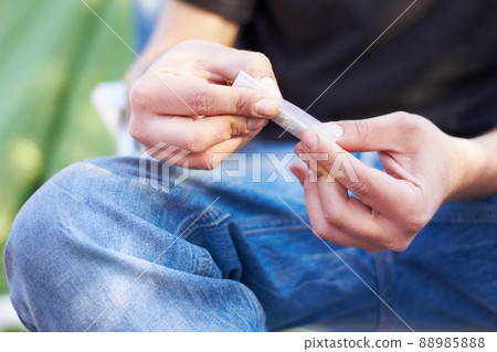 Everything has a gateway. Shot of a unrecognizable person rolling a large marijuana joint. 88985888