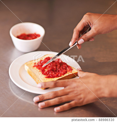 Fruity treat for breakfast. Cropped shot of a woman spreading fruity jam onto toast. 88986310